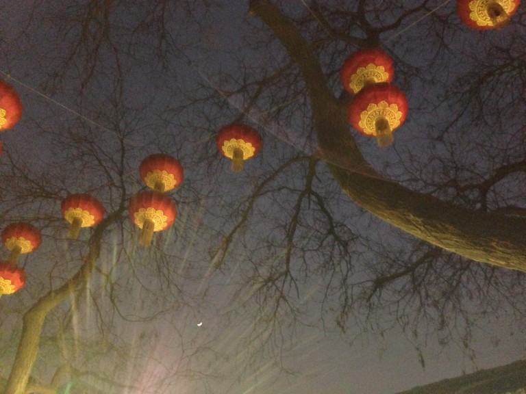 Lanterns dance with a crescent moon silver above the night market in the neighborhood Nanluogu Xiang. 